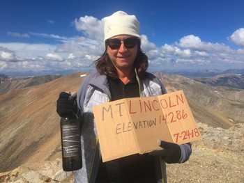 Kim Brown atop Mt Lincoln with bottle of Quandary wine